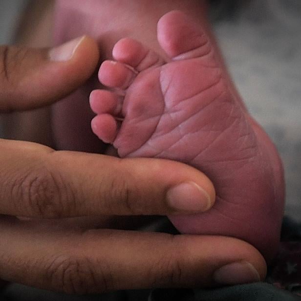 Die Hand eines Erwachsenen hält einen kleinen Babyfuß.