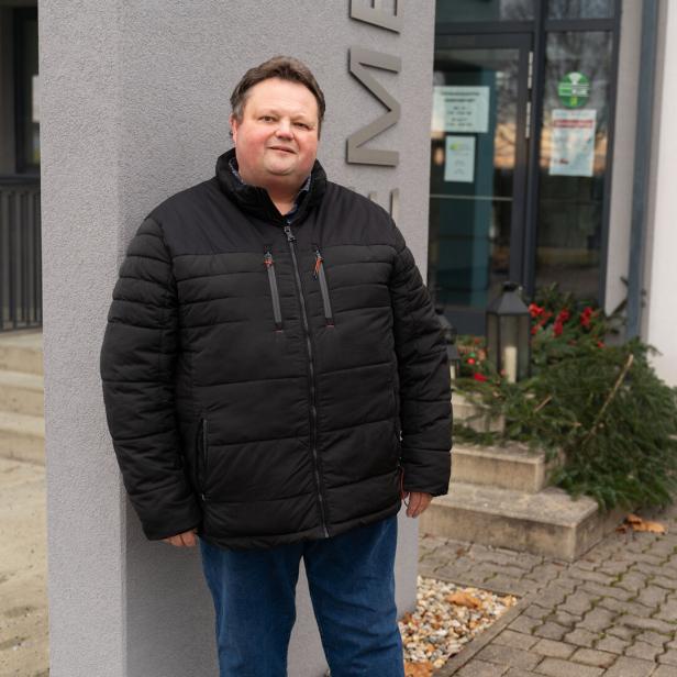 Ein Mann in Winterjacke steht vor einem Gebäude.