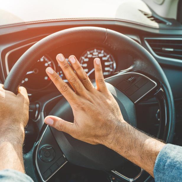 Eine Person betätigt die Hupe in einem Auto.