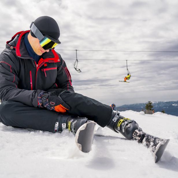 Ein Mann sitzt mit einer Beinprothese auf einer Skipiste.