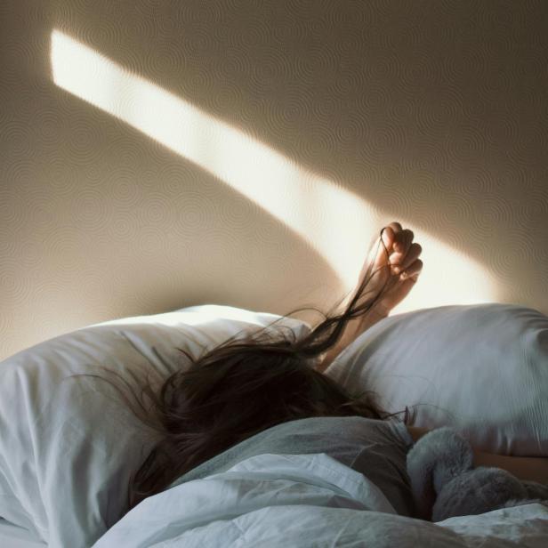 Eine Frau liegt im Bett, während ein Sonnenstrahl an der Wand entlangscheint.