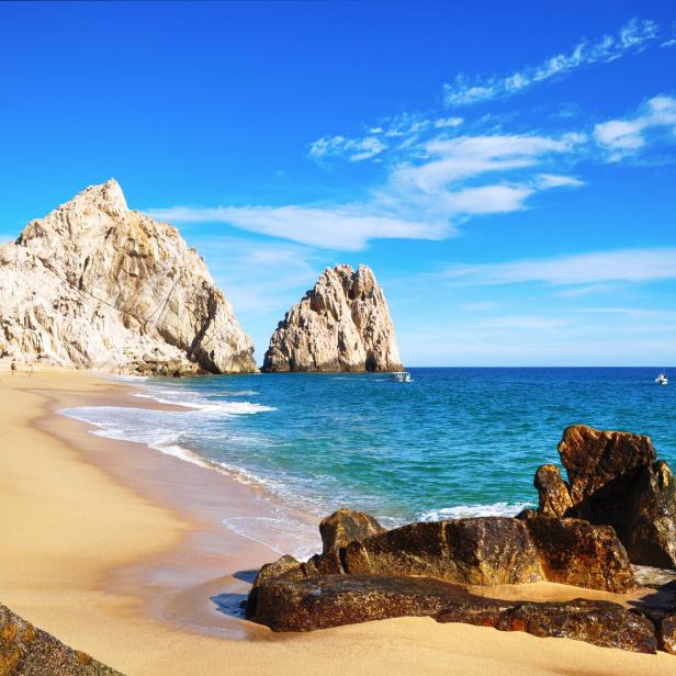 Ein sonniger Strand mit Felsformationen und türkisfarbenem Wasser.