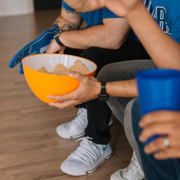 Zwei Männer in blauen T-Shirts schauen ein Spiel und essen Tortilla-Chips.