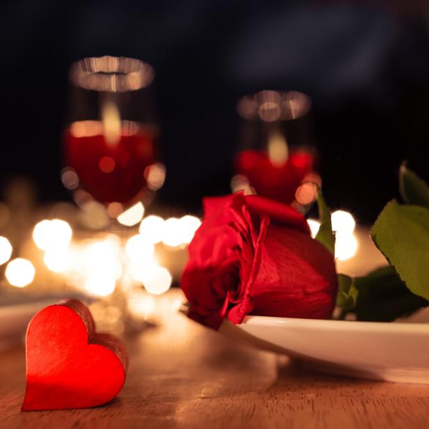 Eine rote Rose und ein Herz auf einem Tisch mit Kerzenlicht.