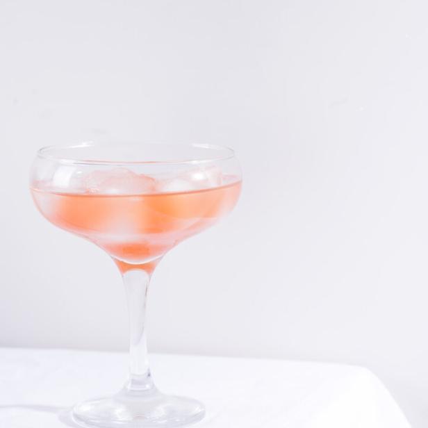 Ein Cocktail mit Eiswürfeln in einem eleganten Glas auf einem weißen Tuch.