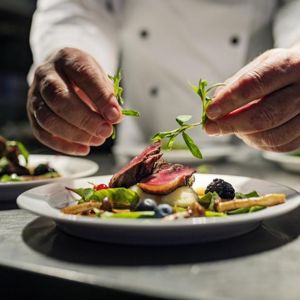 Ein Koch garniert ein Gericht mit Fleisch, Beeren und Gemüse.