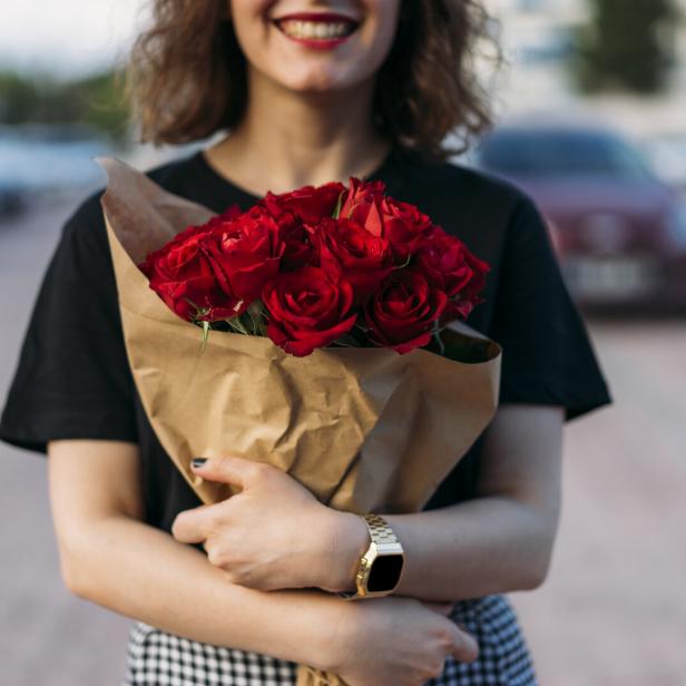 Eine Frau hält einen Strauß roter Rosen in den Armen.