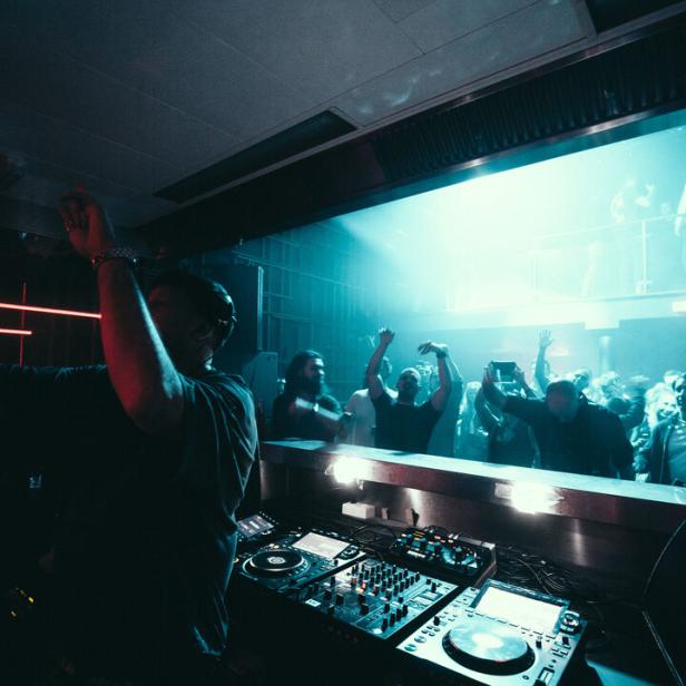 Ein DJ legt in einem Club vor einer jubelnden Menge auf.