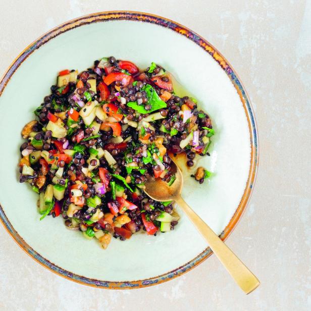 Ein Teller Linsensalat mit Gemüse und einem goldenen Löffel.