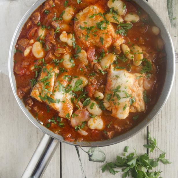 Ein Eintopf mit Fisch, Bohnen und Tomaten wird in einer Pfanne serviert.