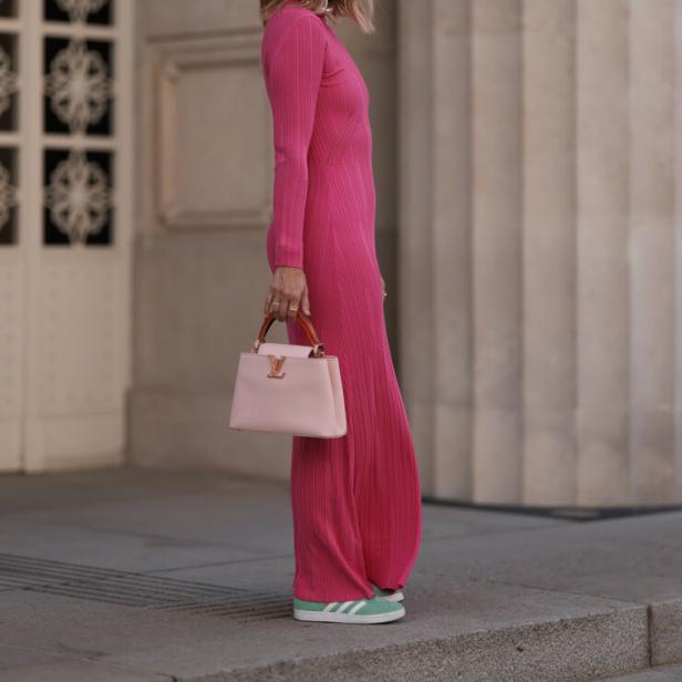 Eine Frau in einem pinkfarbenen Kleid mit einer hellrosa Louis Vuitton Handtasche und grünen Adidas-Sneakers.