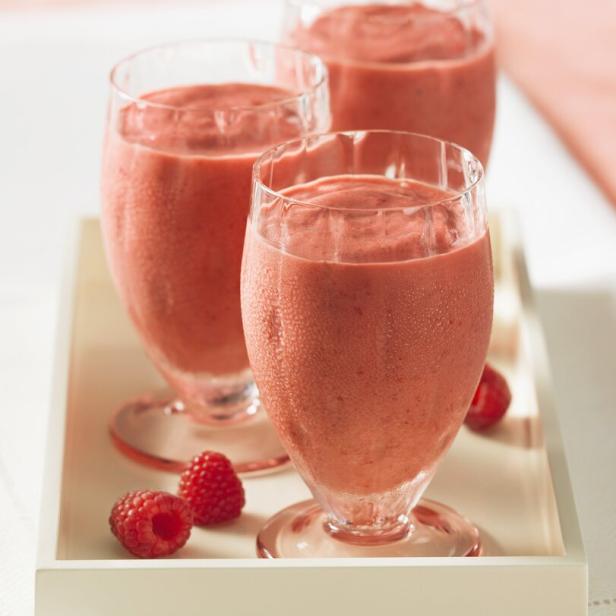Drei Gläser mit Himbeer-Smoothies auf einem weißen Tablett, garniert mit frischen Himbeeren.
