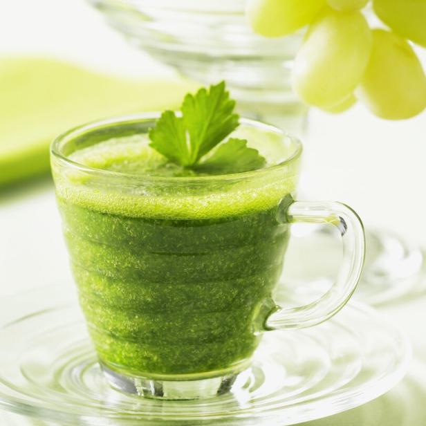 Ein Glas grüner Smoothie, garniert mit einem Petersilienblatt, steht auf einem Tisch.