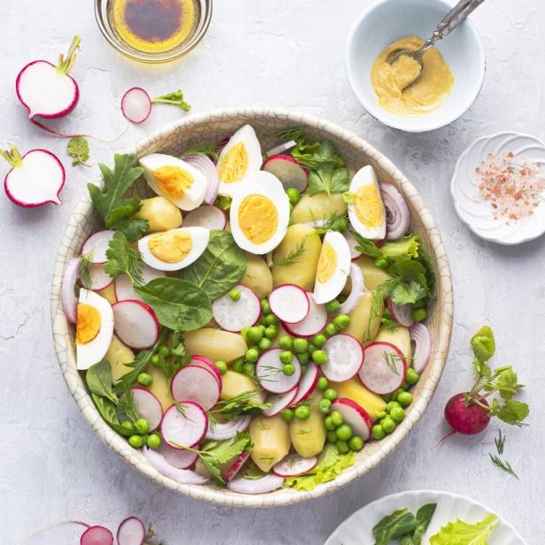 Ein Kartoffelsalat mit Radieschen, Erbsen, Eiern und roten Zwiebeln in einer Schüssel.