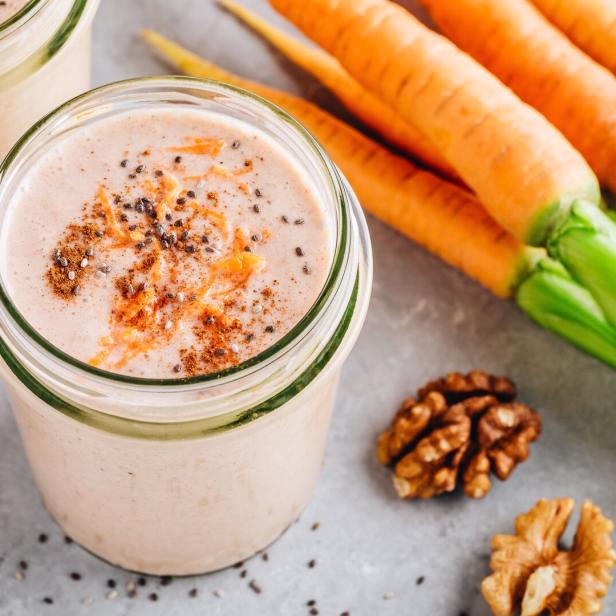 Zwei Gläser Karotten-Smoothie mit Zimt, Chia-Samen und Walnüssen garniert.