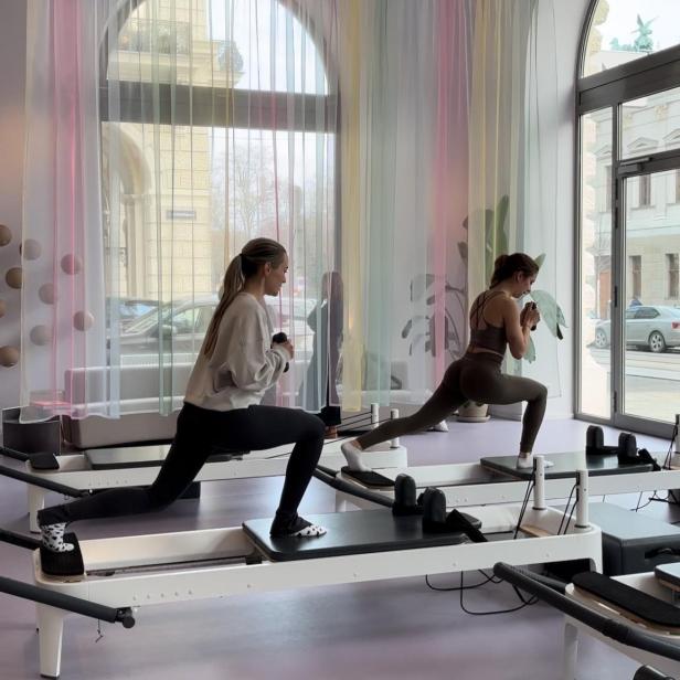 Zwei Frauen trainieren auf Pilates-Reformern in einem hellen Studio.