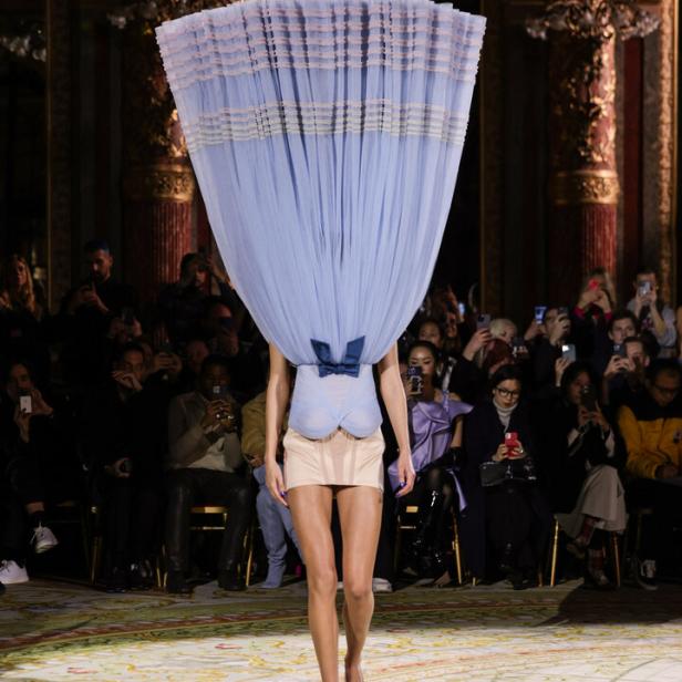 Ein Model mit einem großen, hellblauen Tüll-Hut auf dem Laufsteg.