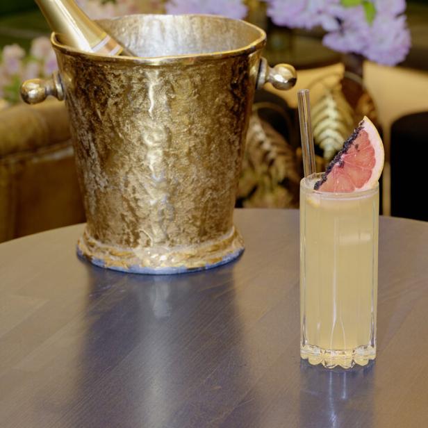 Ein „Century Paloma“-Cocktail neben einem goldenen Champagnerkühler.