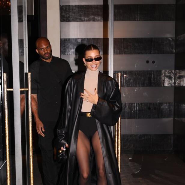 Hailey Bieber verlässt ein Gebäude in einem schwarzen Ledermantel und einer Strumpfhose.