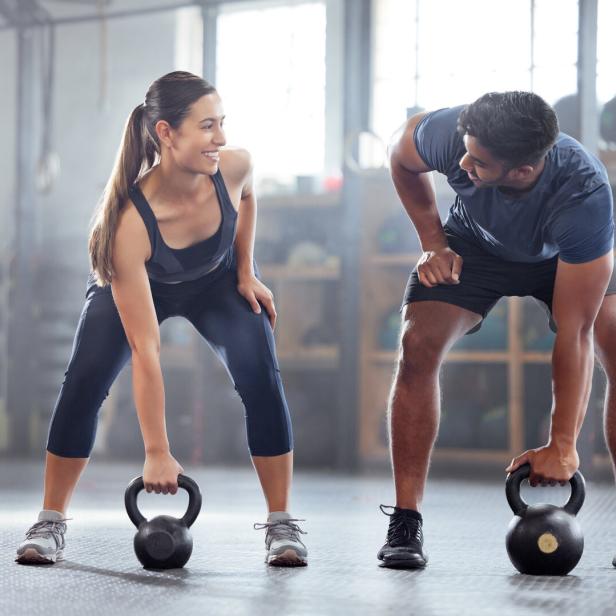 Eine Frau und ein Mann trainieren mit Kettlebells in einem Fitnessstudio.