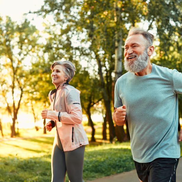 Ein älteres Paar joggt lächelnd in einem sonnigen Park.
