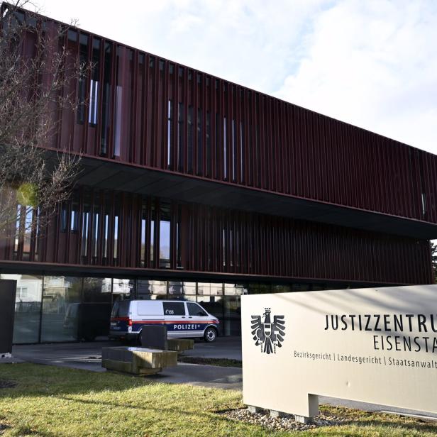 Modernes Justizzentrum mit brauner Fassade, davor ein Polizeiauto und ein Schild mit der Aufschrift „Justizzentrum Eisenstadt“.