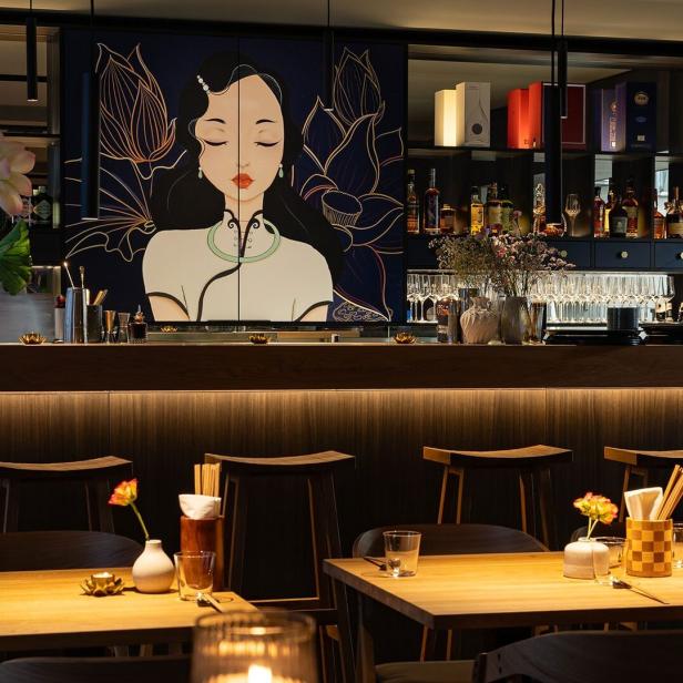 Einrichtung eines Restaurants mit einem Wandbild, das an „Miss Saigon“ erinnert.