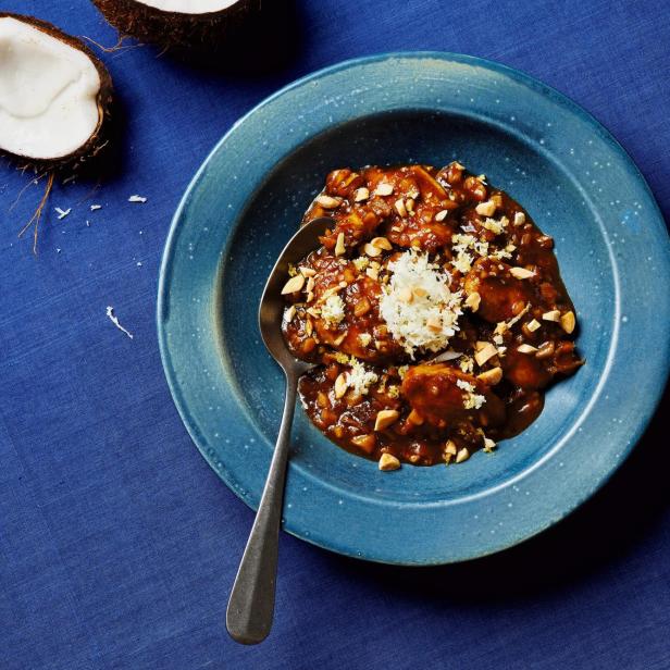 Hähnchen-Kokos-Curry auf einem blauen Teller mit Kokosnussstücken im Hintergrund.
