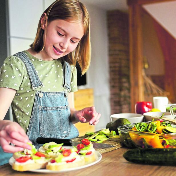 Ein Mädchen richtet Brötchen mit Gemüse an. 