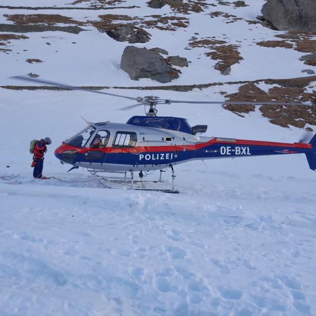 Ein Mann steht neben einem Polizei-Hubschrauber in einer verschneiten Berglandschaft.