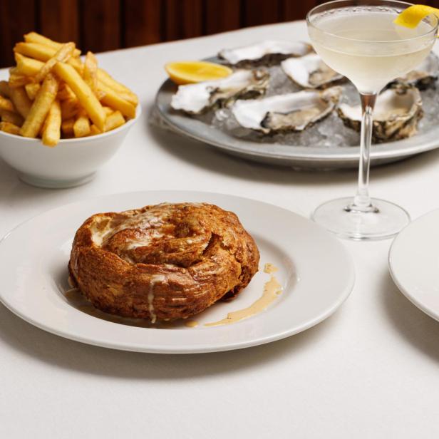 Ein Tisch mit Austern, Pommes Frites, einem Cocktail und einem gefüllten Brötchen.