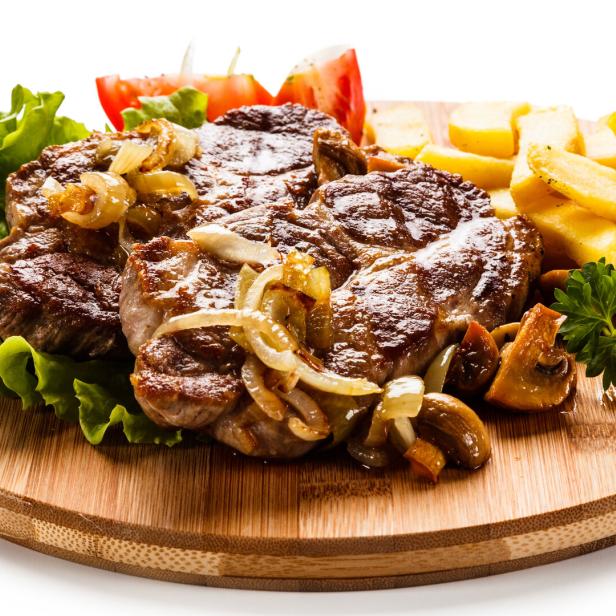 Ein Teller mit Steak, Zwiebeln, Pommes und Salat auf einem Holzbrett.