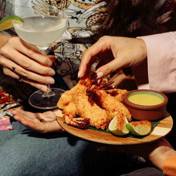 Personen teilen sich panierte Garnelen mit Limetten und einem Dip, dazu ein Cocktail.