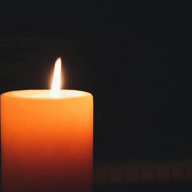 Gelbe Kerze brennt vor dunklem Hintergrund.