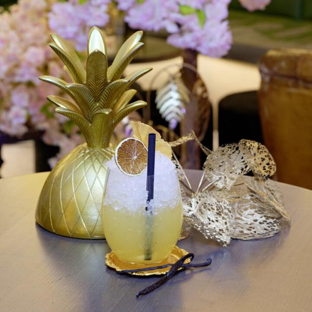 Ein Cocktail mit Eis und einer Orangenscheibe auf einem Tisch mit einer goldenen Ananasdekoration.