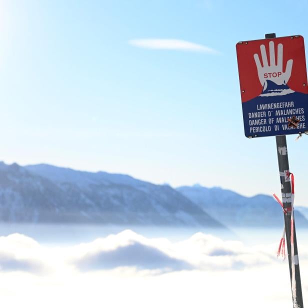 Ein Lawinengefahr-Schild steht vor einer verschneiten Berglandschaft.
