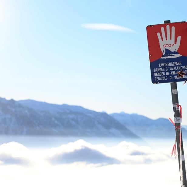 Ein Lawinengefahr-Schild steht vor einer verschneiten Berglandschaft.