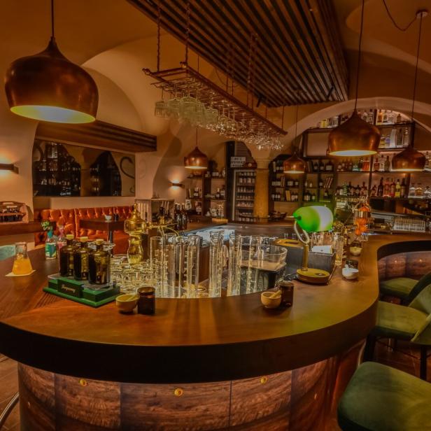 Eine Bar mit dunklen Holzmöbeln und grünen Samtstühlen unter warmem Licht.