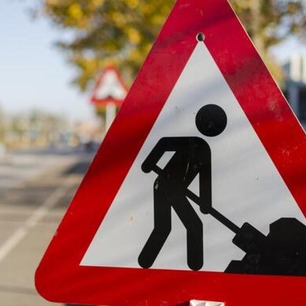 Ein rot-weißes Warnschild kündigt Bauarbeiten an der Straße an.