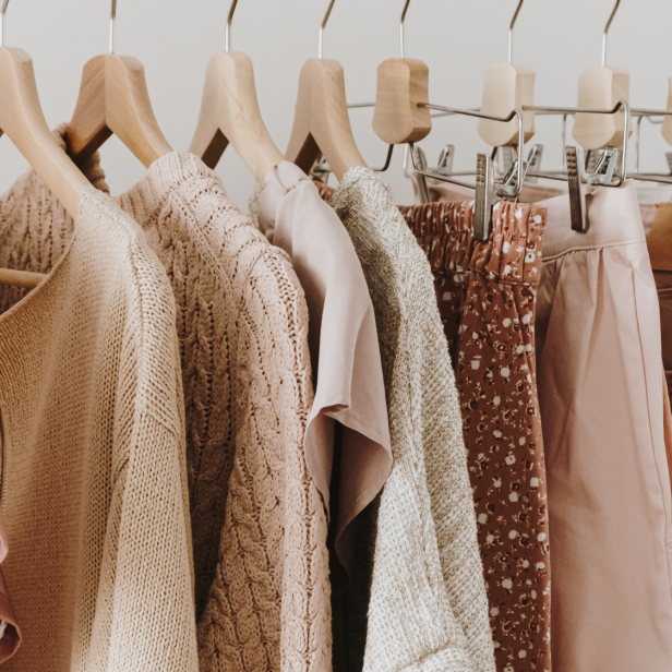 Eine Kleiderstange mit verschiedenen Kleidungsstücken in Rosa-, Beige- und Grautönen.