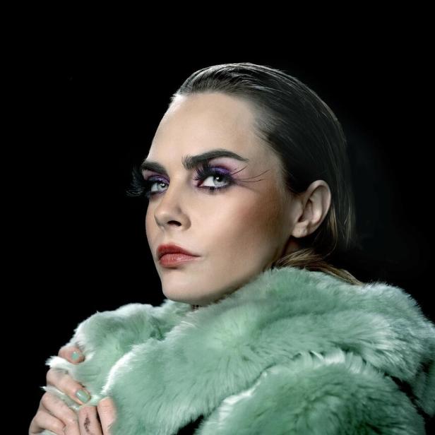 Cara Delevingne trägt einen mintgrünen Pelzmantel und auffälliges Augen-Make-up.