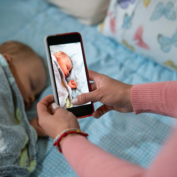 Eine Person fotografiert mit einem Smartphone ein schlafendes Baby.