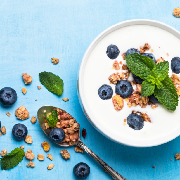 Joghurt mit Blaubeeren, Müsli und Minze auf einem blauen Tisch.