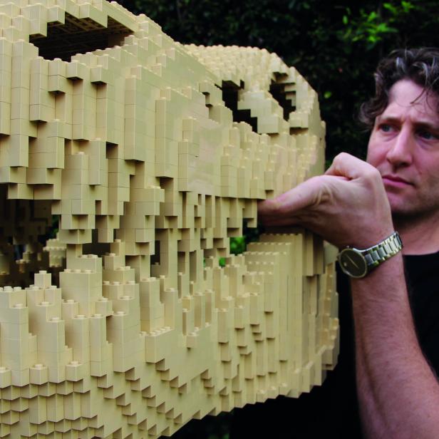 Ein Mann berührt einen Dinosaurierschädel, der aus hellbeigen Legosteinen gebaut wurde.