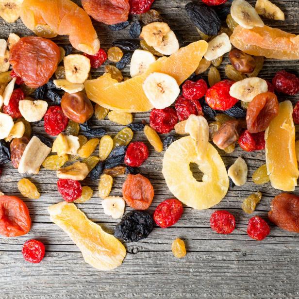 Verschiedene Trockenfrüchte wie Ananas, Mango, Aprikosen, Bananen und Rosinen liegen auf einem Holztisch.