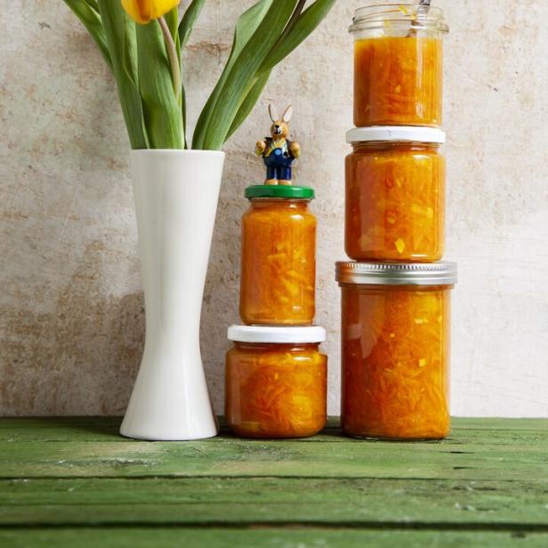 Gelbe Tulpen in einer Vase neben gestapelten Gläsern mit Orangenmarmelade.