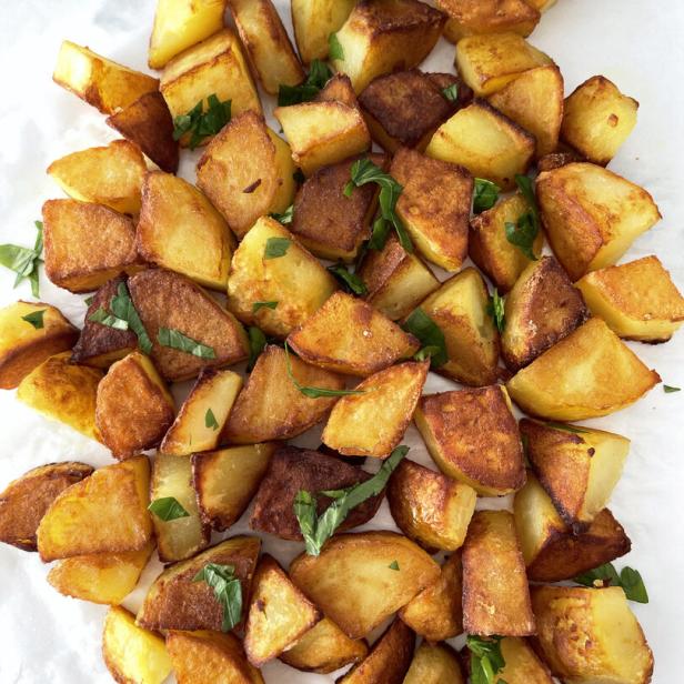 Gebratene Kartoffelstücke, garniert mit frischen Kräutern, liegen auf einem weißen Untergrund.