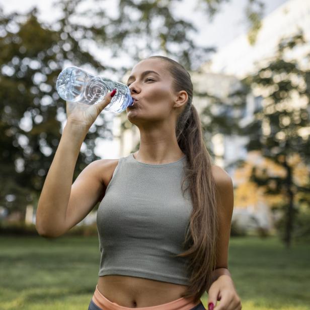 Eine junge Frau trinkt im Park aus einer Wasserflasche.