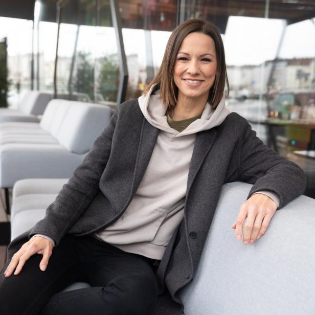 Christina Stürmer sitzt lächelnd auf einem Sofa.