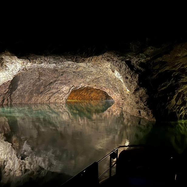 Eine dunkle Grotte mit grünlichem Wasser wird von Felswänden und schwachem Licht umgeben.